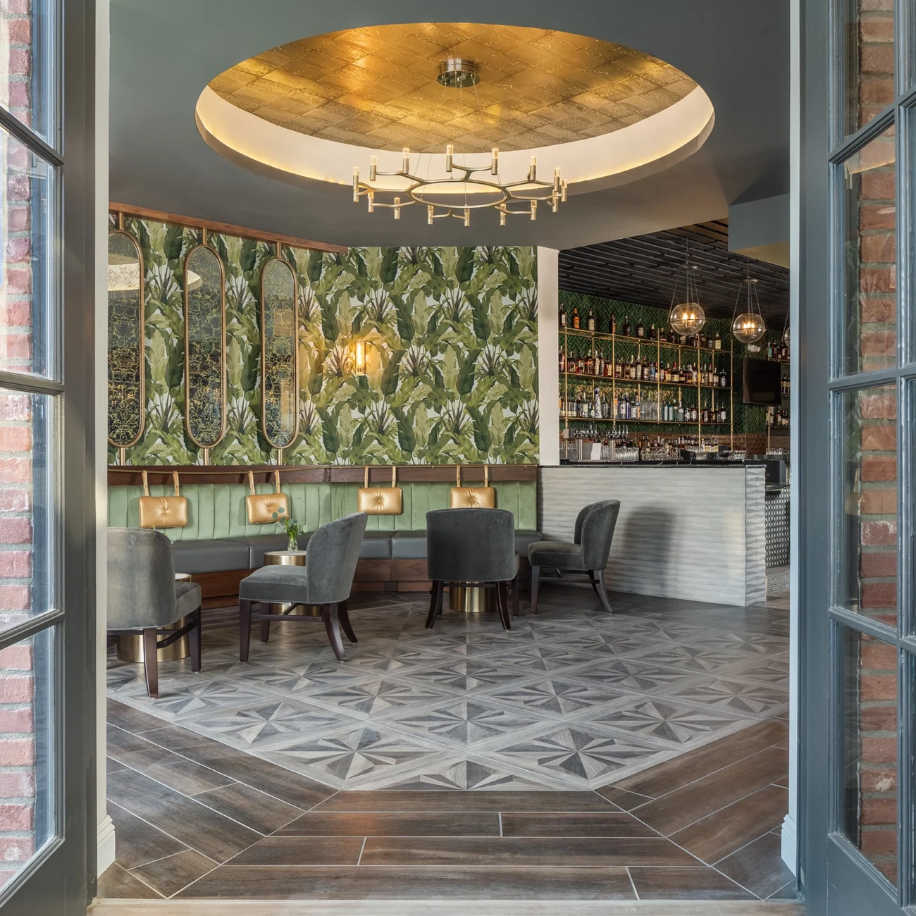 Christine Vroom Interiors Pacific Standard | Contemporary Restaurant Interior with luxury dining area, large palm wallpaper, gold framed mirrors, velvet seating, vaulted ceiling and parquet flooring